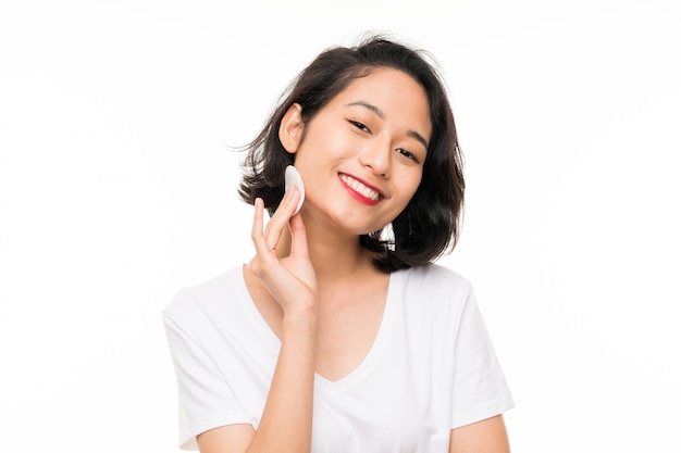 Aziatische jonge vrouw die make-up verwijdert uit haar gezicht met wattenschijfje