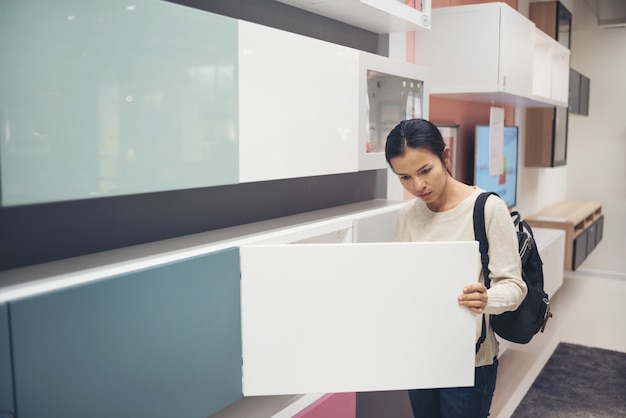 Aziatische jonge vrouw die meubilair in een moderne opslag van het huismeubilair kiezen