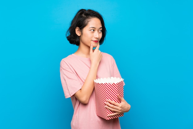 Aziatische jonge vrouw die popcorns eet die een idee denkt