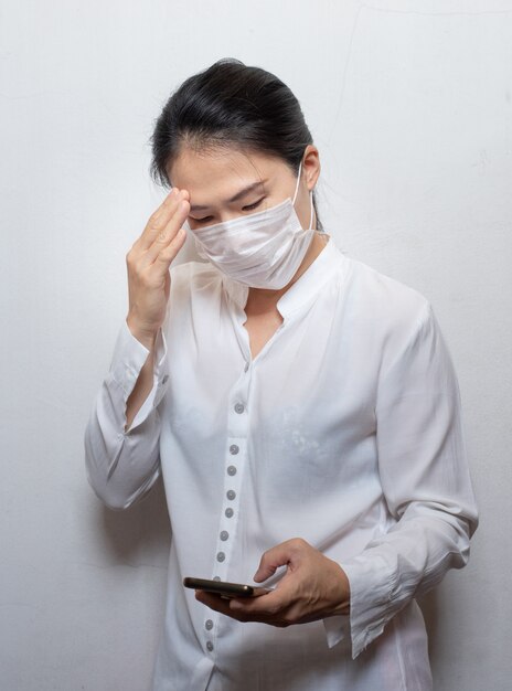 Aziatische jonge vrouw die slimme telefoon met behulp van gezichtsmasker dragen