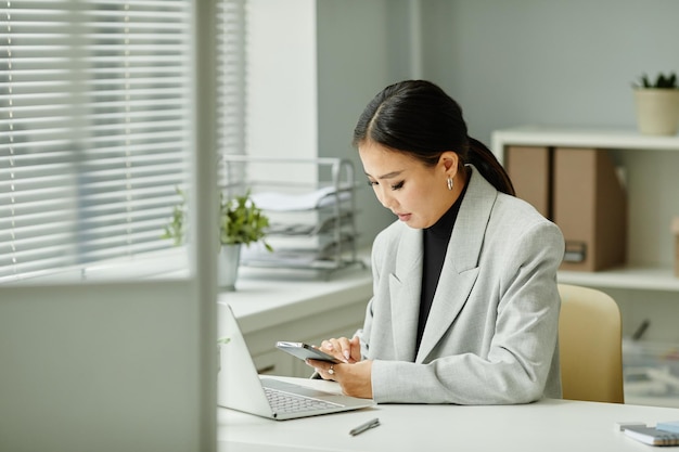 Aziatische jonge vrouw die smartphone gebruikt op de werkplek