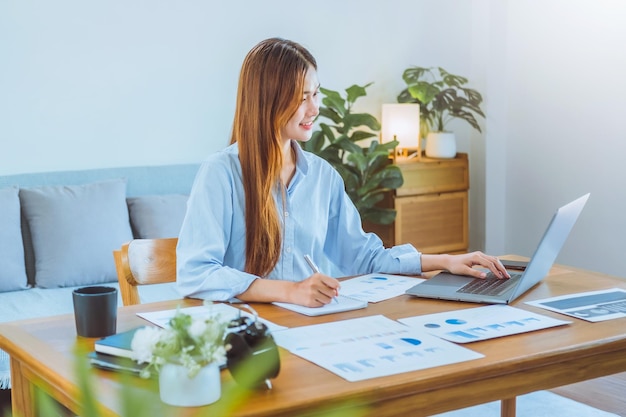 Aziatische jonge vrouw die thuis werkt met behulp van computer en koffie drinkt in haar kamer, documentfinanciering en online conferentievergadering voor nieuwe projecten