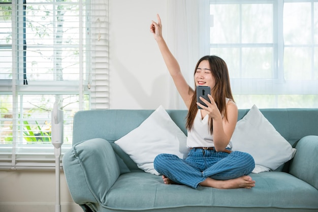 Aziatische jonge vrouw draagt oordopjes luisteren naar muziek op de bank met slimme mobiele telefoon in de huiskamer Levensstijl vrouwelijke draadloze oortelefoons chill een beetje dansen van muziekapplicatie smartphone