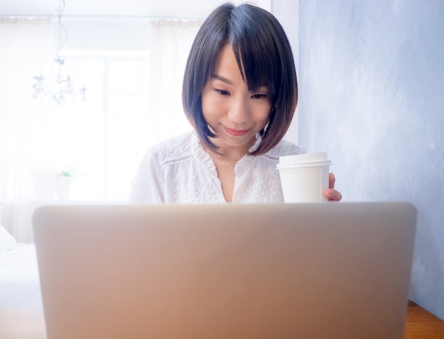 Aziatische jonge vrouw drinkt voor laptop