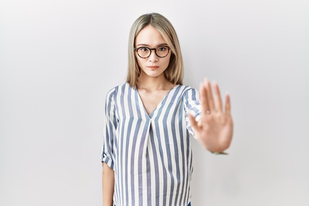 Aziatische jonge vrouw, gekleed in vrijetijdskleding en een bril, doet stoppen met zingen met de palm van de hand. waarschuwende uitdrukking met een negatief en serieus gebaar op het gezicht.