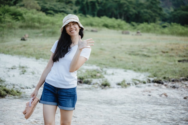 Aziatische jonge vrouw genieten van en ontspannen met de natuur, gebied van waterstroom, waterval buiten