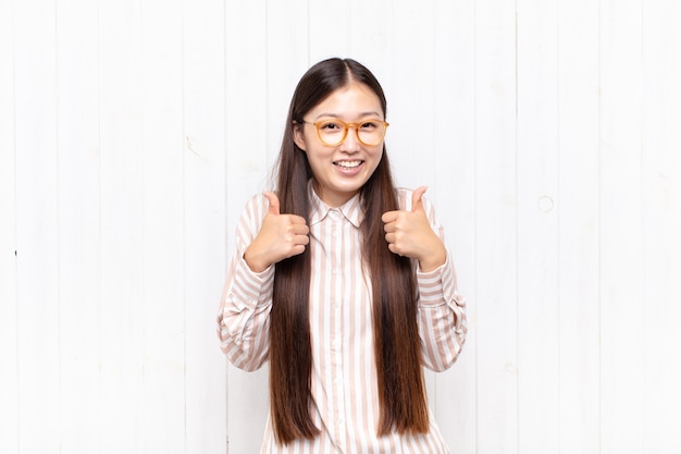 Aziatische jonge vrouw glimlachend in grote lijnen op zoek gelukkig, positief geïsoleerd
