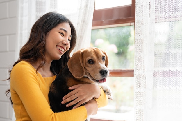 Aziatische jonge vrouw in casual kleding knuffelen haar beagle hond zittend in de woonkamer thuis