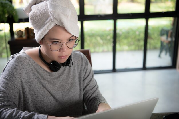 Aziatische jonge vrouw in vrijetijdskleding gebruikend laptop en glimlachend terwijl het werken van huis