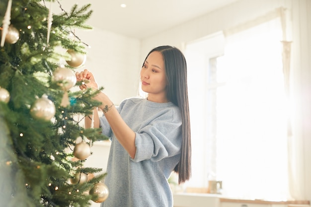 Aziatische jonge vrouw kerstballen opknoping op kerstboom en vakantie voorbereiden