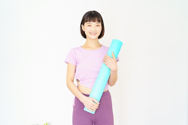 Aziatische jonge vrouw met yogamat binnenshuis