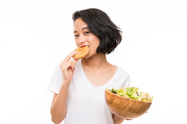 Aziatische jonge vrouw over geïsoleerde muur met salade en doughnut