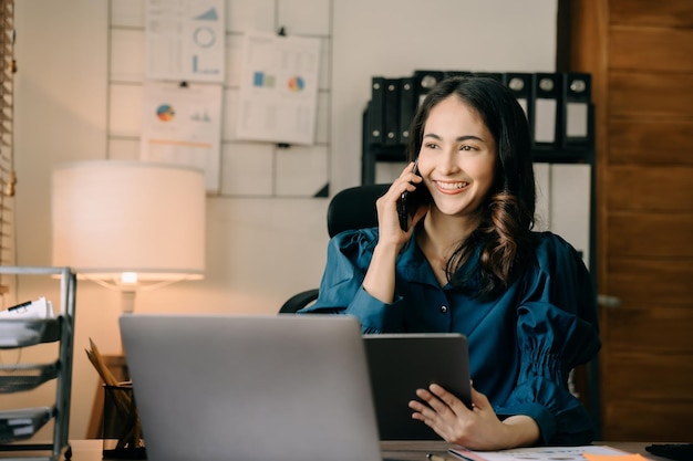 Aziatische jonge vrouw praat over mobiele telefoons en werkt op laptopcomputers online telewerkconcept voor bedrijven