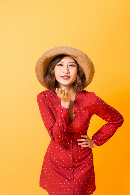 Aziatische jonge vrouw stuurt luchtkus Meisje draagt rode jurk en bruine hoed over oranje achtergrond
