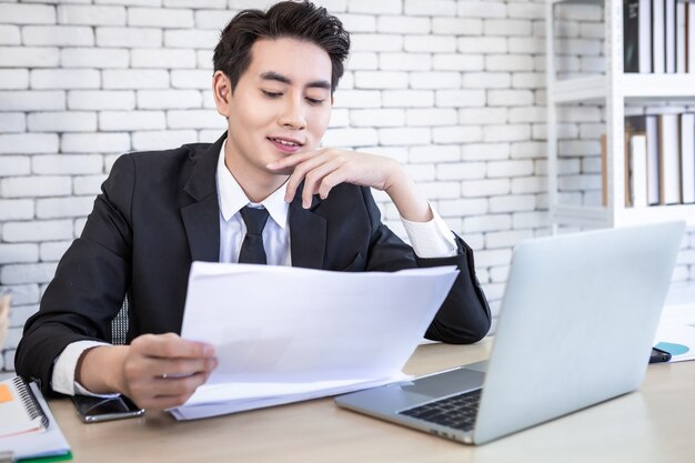 Aziatische jonge zakenman heeft de nadruk gelegd op het zien van een document-businessplan en laptopcomputer op houten tafel na zakelijke verliezen op de achtergrond van de kantoorruimte.