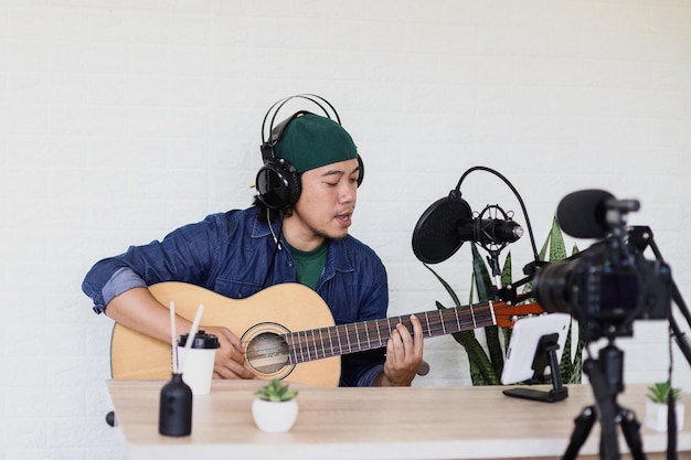 Aziatische jongeman in casual stijl zingt en speelt gitaar op muziekpodcast