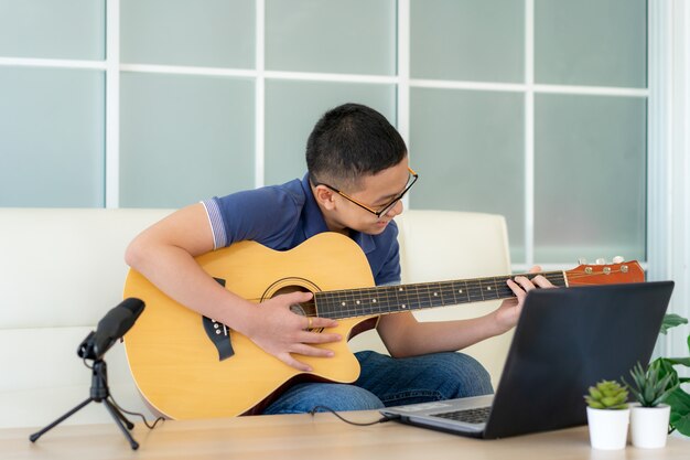 Aziatische jongen die akoestische gitaar speelt en op online cursus op laptop let