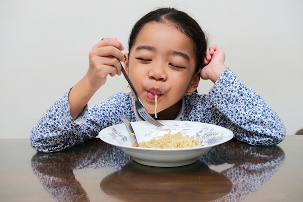 Aziatische jongen die blije uitdrukking toont bij het eten van noedels