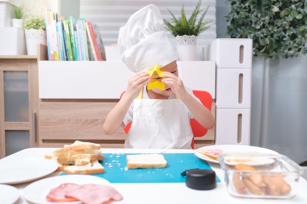 Aziatische jongen die chef-kokhoed en schort draagt tijdens het koken