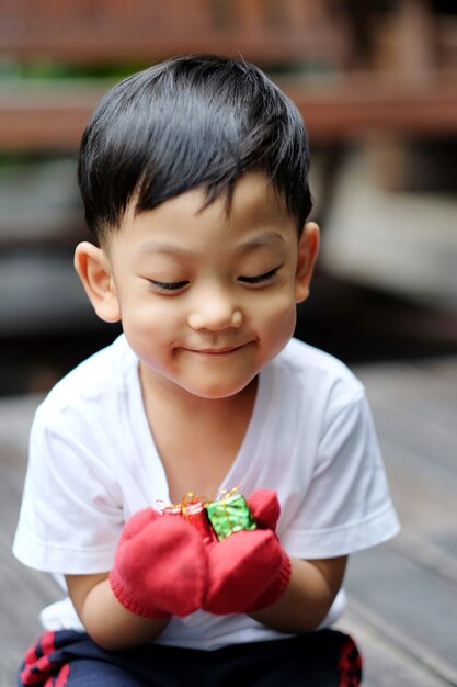 Aziatische jongen die de rode handschoenen draagt ​​en de kleine huidige doos houdt