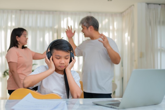 Aziatische jongen die een koptelefoon draagt en luide muziek speelt om geen ruzie te horen terwijl de ouders