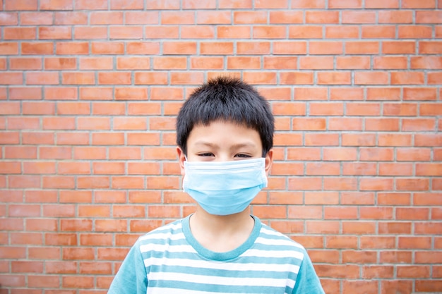 Foto aziatische jongen die een maskerbakstenen muur draagt als achtergrond.