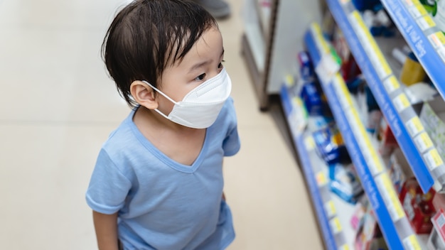 Aziatische jongen die gezichtsbescherming in preventie voor virus in supermarkt draagt