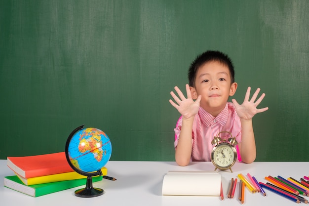 Aziatische jongen die hand toont en in schoolbordruimte leert