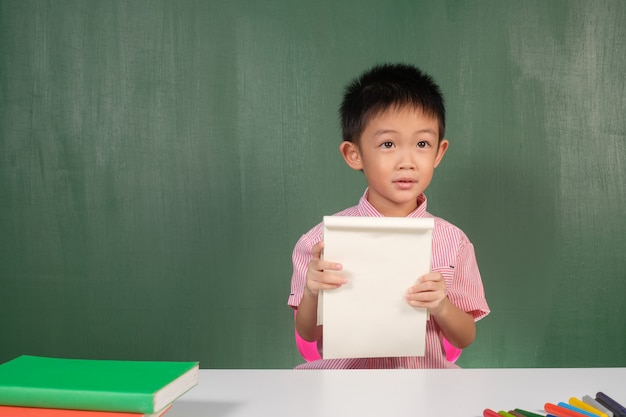 Aziatische Jongen die leeg notitieboekje in schoolbordruimte toont