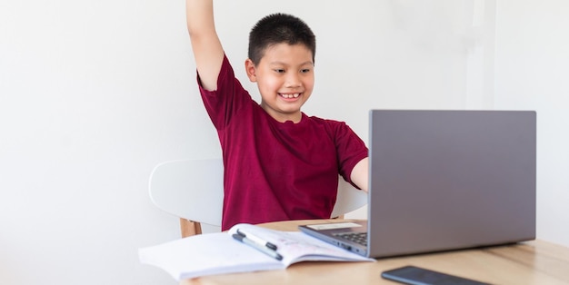 Aziatische jongen die online studeert op een computerlaptop met een lachend en blij gezicht thuis