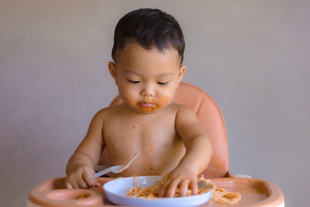 Aziatische jongen die op hoge babystoel eet.