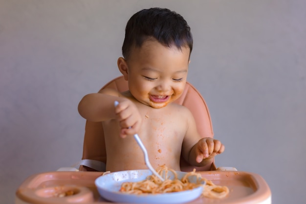 Aziatische jongen die op hoge babystoel eet.