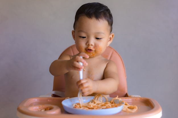 Aziatische jongen die op hoge babystoel eet.