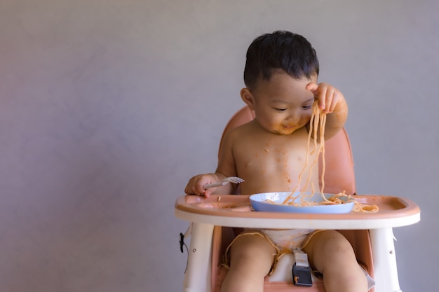 Aziatische jongen die op hoge babystoel eet.