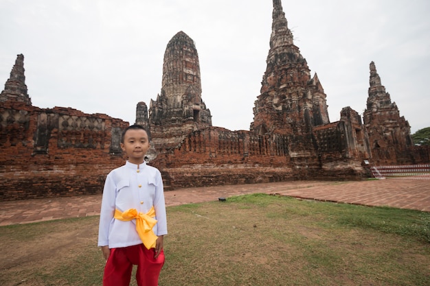 Aziatische jongen die Thaise kleding in oude tempel draagt