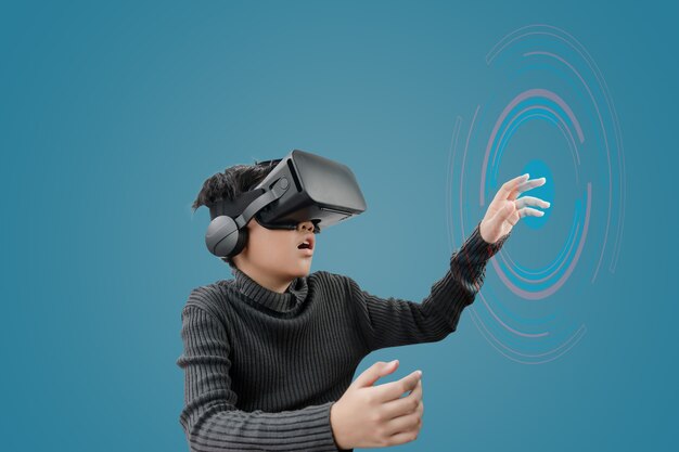 Aziatische jongen die vr-brilhoofdtelefoon draagt met technologiegrafiek vooraan op blauwe kleurenachtergrond.