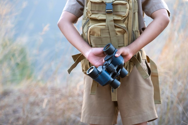 Aziatische jongen in avonturiersjongenskleren die camera en verrekijker voorbereiden op jungletrekking verrekijkers in padvinderswandelingen