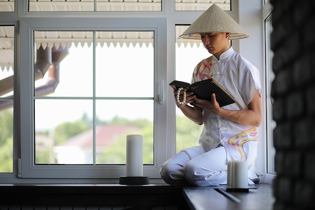 Aziatische jongen in kimono die een oud boek leest dat bij het raam zit