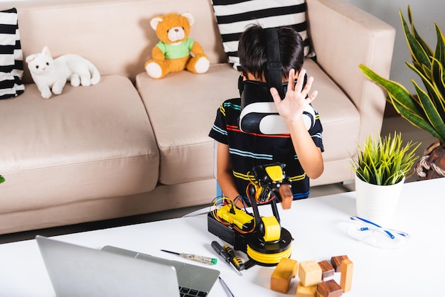 Aziatische jongen jongen met VR-bril op robotarm in werkplaats Kind leren programmeur controle robotarm met sensoren om houtblok op te halen Technologie-onderwijs Virtual Reality Simulator-industrie 40
