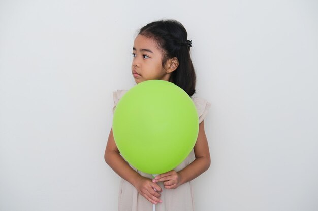 Aziatische jongen kijkt naar de rechterkant met een droevige uitdrukking terwijl hij een groene ballon vasthoudt