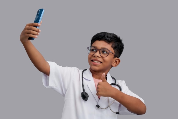 Foto aziatische jongen met een dokter schort met stethoscoop praat selfie met telefoon toont duim omhoog