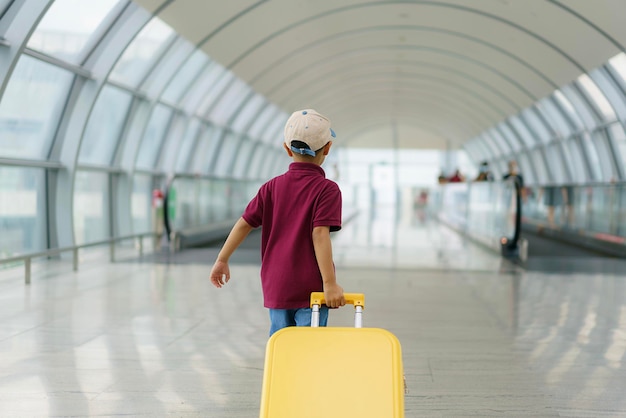 Aziatische jongen met gele koffer draagt hemd en korte broek loopt in de luchthaven terminal