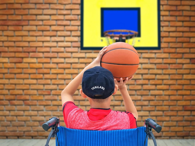 Foto aziatische jongen op rolstoel die basketbal probeert te oefenen na herstel van een gebroken enkelblessure