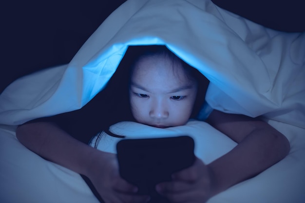 Aziatische jongen speelspel op smartphone in het bed 's nachts The girl Addict social media