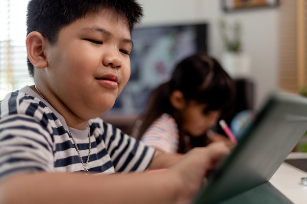 Aziatische jongens en meisjes genieten van online leren door thuis aantekeningen te maken en tablets te gebruiken