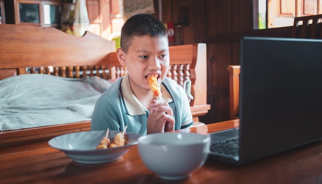 Aziatische jongens eten junkfood terwijl ze thuis aan een bureau zitten met notitieboekjes en laptops