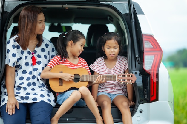 Aziatische kinderen en hun moeder spelen gitaar en zingen samen een lied in de kofferbak van een auto