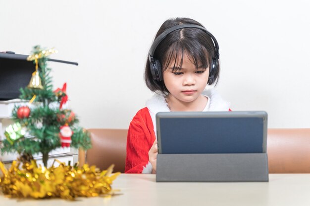 Foto aziatische kinderen meisje jurk kerst santa claus chatten met vrienden op digitale tablet. kerstvakantie concept stock photo