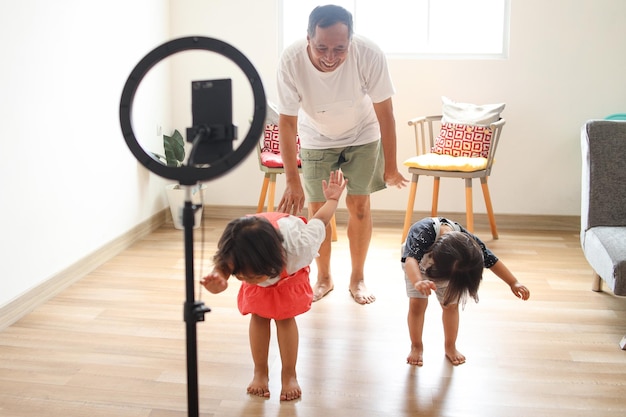 Aziatische kinderen met opa dansen op camera en filmen video met behulp van telefoon op statief thuis