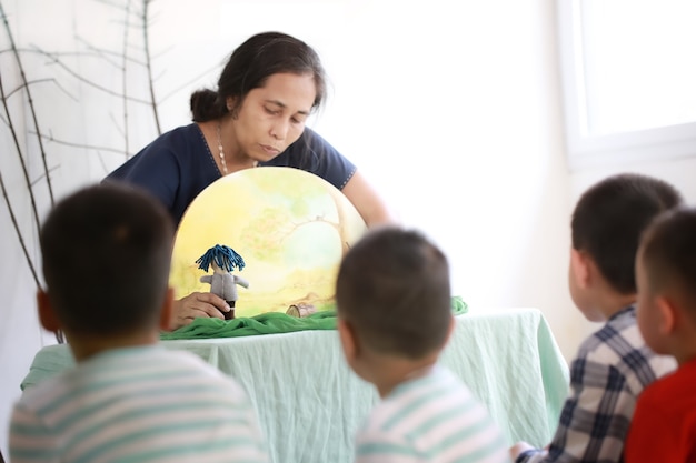 Aziatische kinderen zitten en luisteren naar de leraar die een verhaal vertelt met handgemaakte waldorf-poppen.